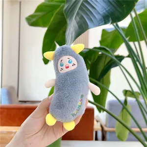 Macro shot of a gray plush chicken keychain with RAINBOW embroidery and plant backdrop