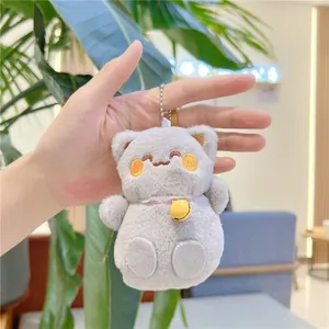 Dettaglio di un ciondolo a forma di gatto di peluche grigio con campanellino rosa e catenina