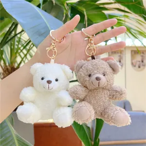 Close-up of curly plush teddy bear keychains in white and light brown held by a hand