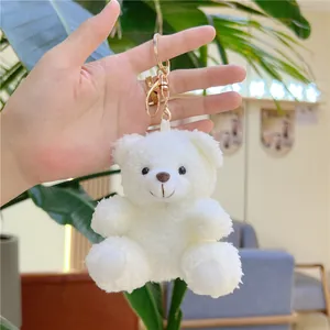 Close-up of white plush teddy bear keychain with gold metal buckle held by hand