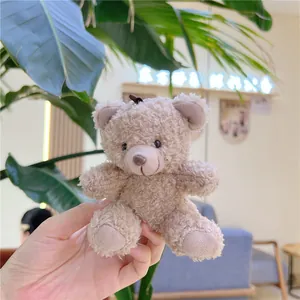 Close-up of a curly teddy bear plush keychain with a brown strap held in hand