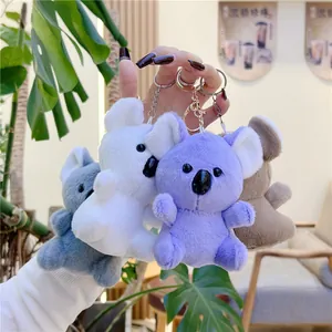 Plush koala keychains in four colors held by a model in a cozy cafe setting