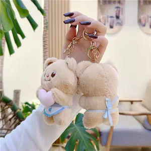 Cute brown plush bear keychain with pink heart and blue bow in hand-held lifestyle shot