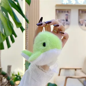 Cute green plush dolphin keychain with golden chain held against a cozy indoor background
