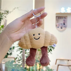 Cute croissant plush keychain with smiley face and long legs held by hand