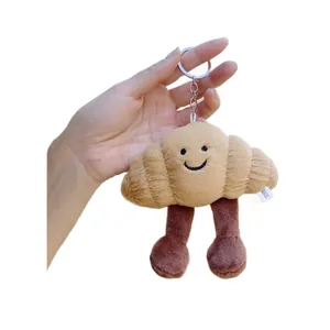 Cute croissant plush keychain featuring a smiling face and small legs on white background