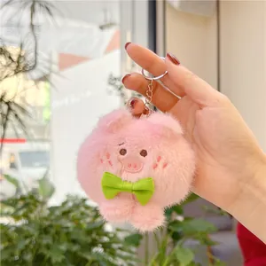 Schattige roze pluche varkenssleutelhanger met groene strik in de hand