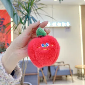 Detailed view of a soft red plush apple keychain with embroidered face and green leaf