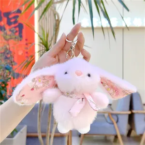 Close-up of pink plush bunny keychain with floral ears and scarf on a silver ring