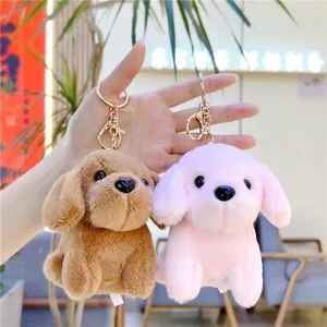 Cute plush puppy keychains in brown and pink colors held by hand in a warm indoor setting
