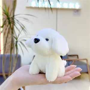 Close-up of small white plush puppy keychain in palm showing soft furry texture