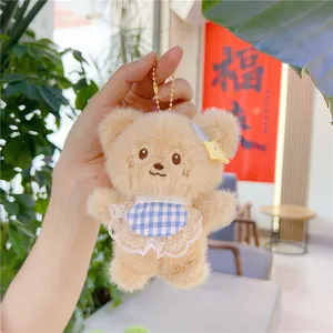 Close-up of plush bear keychain with blue plaid apron and lace trim held by hand