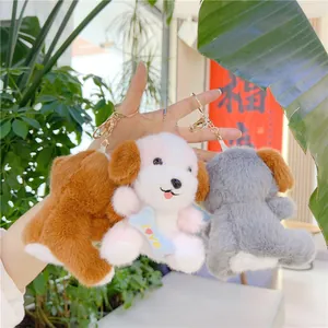 Llavero de perro de peluche en marrón, rosa y gris con clips dorados sostenido a mano