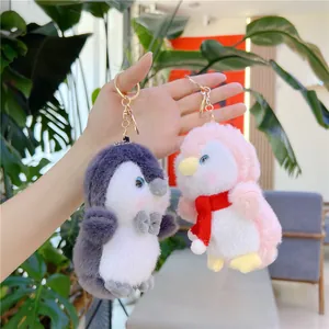 Detailed close-up of soft gray and pink plush penguin keychains with gold metal clasps
