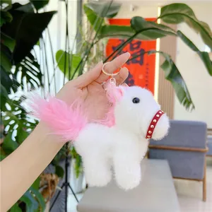 White plush pony keychain with pink mane and gold ring held in hand for mascot display