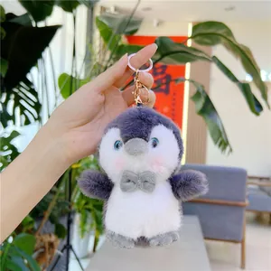 Close-up of a cute plush penguin keychain with soft grey fur and a golden metal clasp