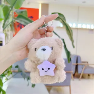 Close-up of a plush bear keychain holding a purple star, shown in hand for scale