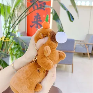 Close-up of cute plush capybara keychain with orange decor and golden metal ring