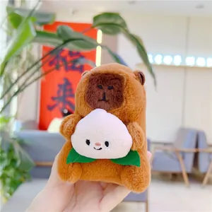 Macro detail of plush capybara pendant holding a peach with embroidered smile