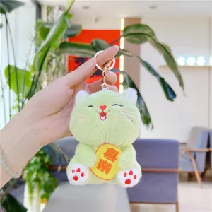 Close-up of green plush cat keychain holding a yellow tag with embroidery detail