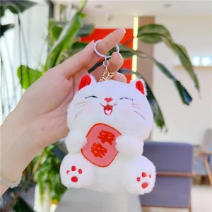 Close-up of white plush fortune cat keychain holding a red sign with peace characters