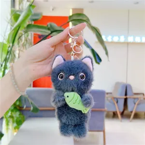 Close-up of a grey plush cat keychain holding a green fish with golden metal lobster clasp