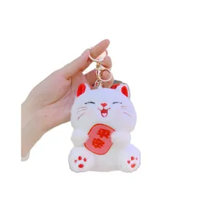 White plush lucky cat keychain holding a Ping An blessing charm with gold metal clasp