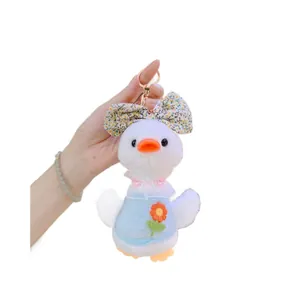 Cute plush duck keychain with floral bow and blue outfit held by hand for scale