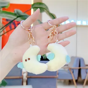 Pair of plush crescent moon keychains in beige with blue wings and rose gold metal rings