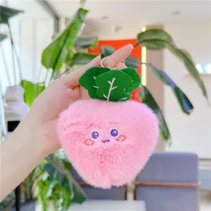 Dettaglio di un portachiavi in peluche rosa con viso ricamato e foglie verdi decorative
