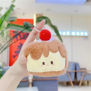 Close-up of cute plush cake keychain with red pom-pom and silver metal clasp held in hand