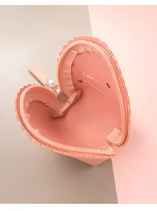 Detalle de cartera rosa en forma de corazón con bordes festoneados y elegante perla decorativa