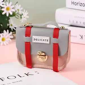 Detail of a mini tri-color crossbody bag with golden lock and DELICATE lettering on pink table