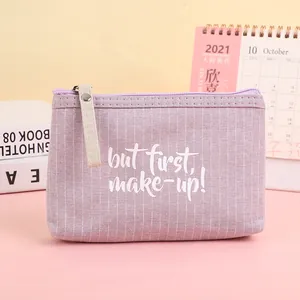 Close-up of purple striped canvas cosmetic bag with 'but first, make-up!' slogan