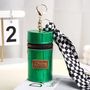 Detail van groen cilindrisch lippenstiftetui met gouden sleutelhanger en lint