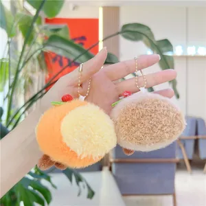 Detail of plush orange fruit pendant and brown berry charm with golden chain on a hand