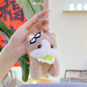 Macro detail of plush cat keychain with heart glasses and green scarf held by hand