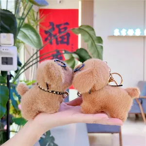 Close-up of two plush puppy keychains with round glasses and bells held by a hand