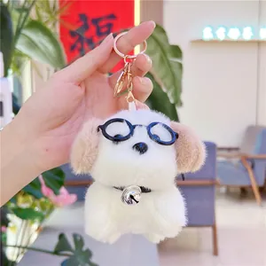 Close-up of white plush dog keychain with black glasses and a silver bell on hand