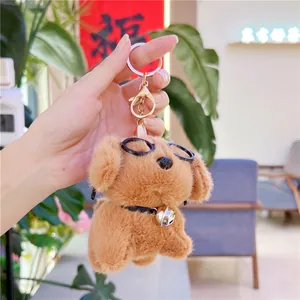 Close-up of a plush brown puppy keychain with black glasses and a silver bell collar