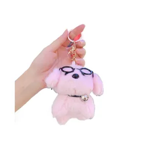 Plush pink puppy keychain with black glasses and gold bell held in hand on white background