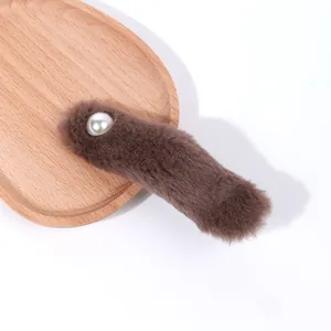 Dettaglio del fermaglio in peluche marrone scuro con perla bianca su vassoio in legno