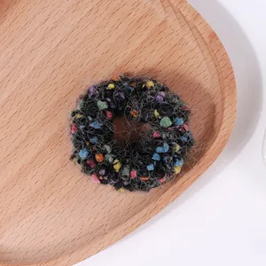 Primer plano de coletero de punto colorido con pompones sobre bandeja de madera