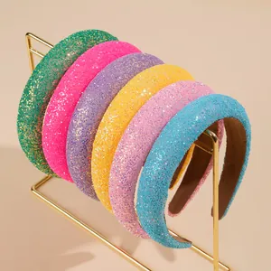 Set of six colorful glitter sponge headbands on a gold display stand with soft background