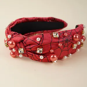 Close-up of red knotted headband with pearls, rhinestones and black spider web pattern