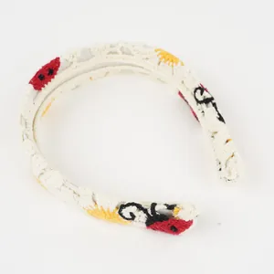 Detailaufnahme des Häkelstirnbands mit Marienkäfer- und Blumenmuster auf elfenbeinfarbenem Stoff