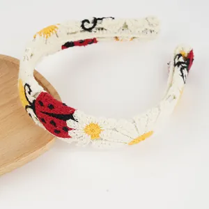 Detaillierte Strickstruktur eines Boho-Stirnbands mit Marienkäfer- und Gänseblümchen-Muster