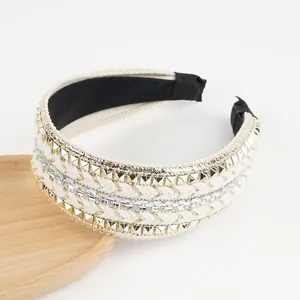 Détail d'un serre-tête tissé beige orné de clous dorés et de strass brillants sur fond blanc