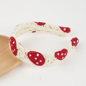 Detail eines gehäkelten Stirnbands mit rotem Pilzmuster auf creme gestricktem Stoff