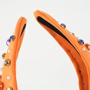 Detailed close-up of orange knotted headband with colorful rhinestones and faux pearls
